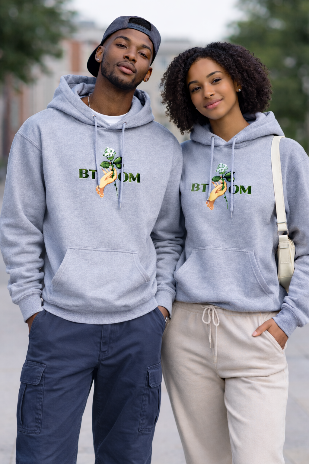 Two people wearing matching gray hoodies with a brand logo outdoors.